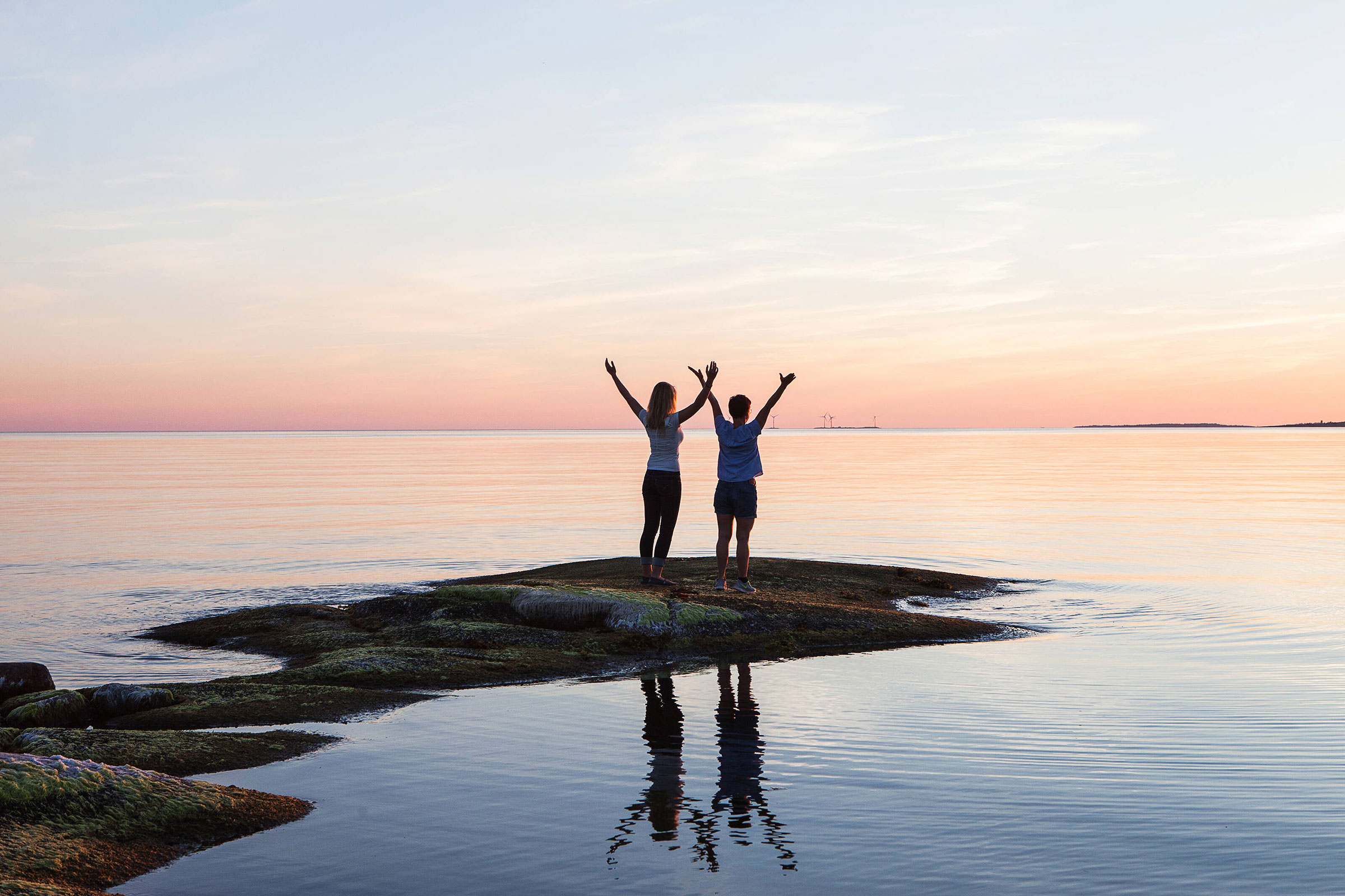 Two people standing towards the sunset with open arms at the sea shore