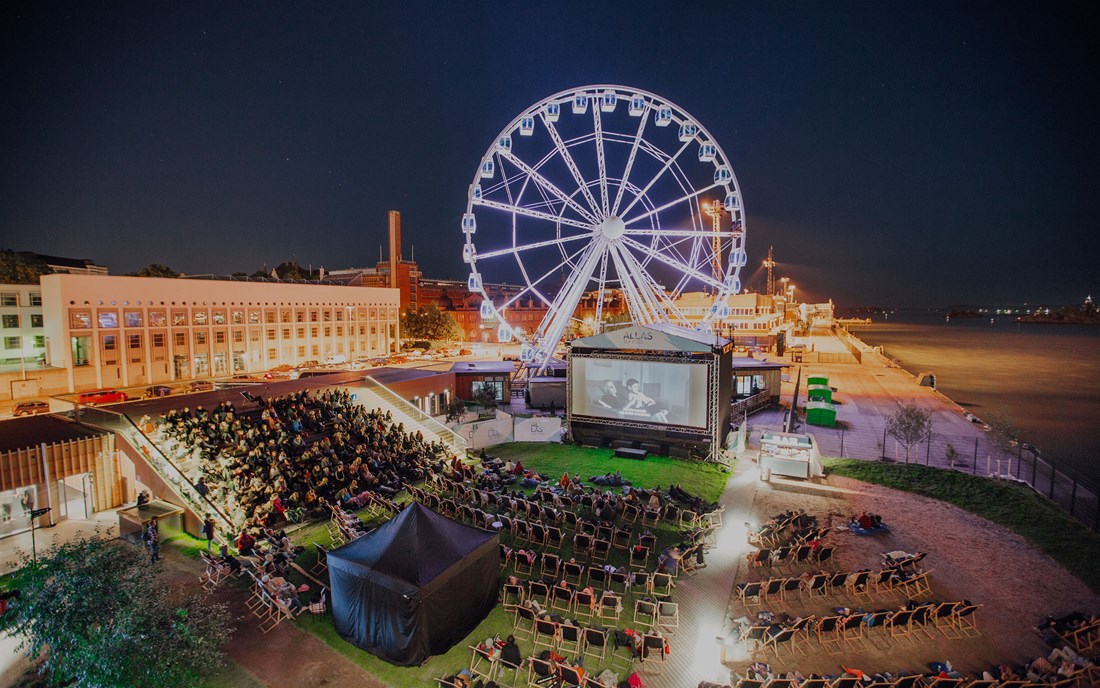 View of Helsinki SkyWheel and an outside cinema with people watching a movie.
